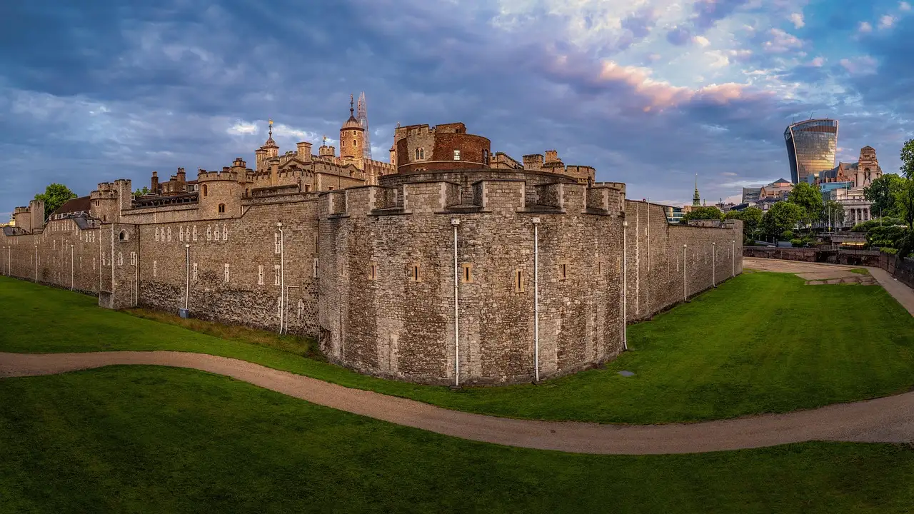 Tower of London fortress walls and towers above a green lawn under an evening sky