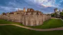 Tower of London fortress walls and towers above a green lawn under an evening sky
