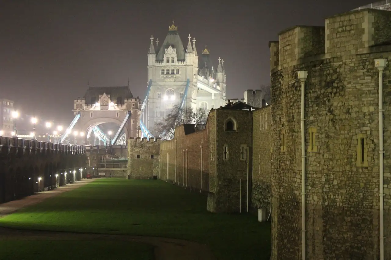 Tower of London walls at night with the lit-up Tower Bridge behind