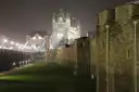Tower of London walls at night with the lit-up Tower Bridge behind