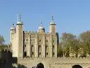 The White Tower of the Tower of London behind its gate, with spring trees and blue sky