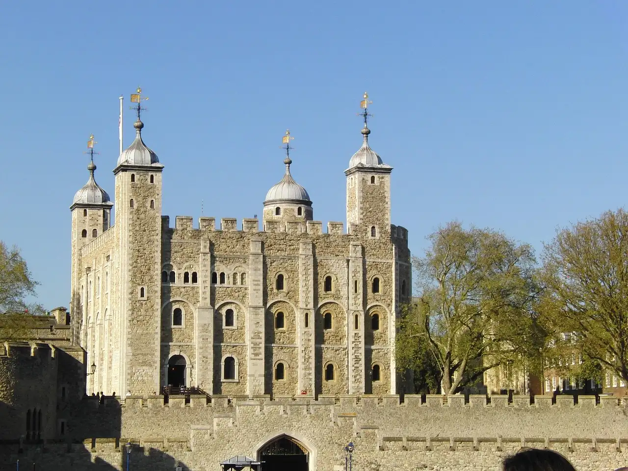 The White Tower of the Tower of London behind its gate, with spring trees and blue sky