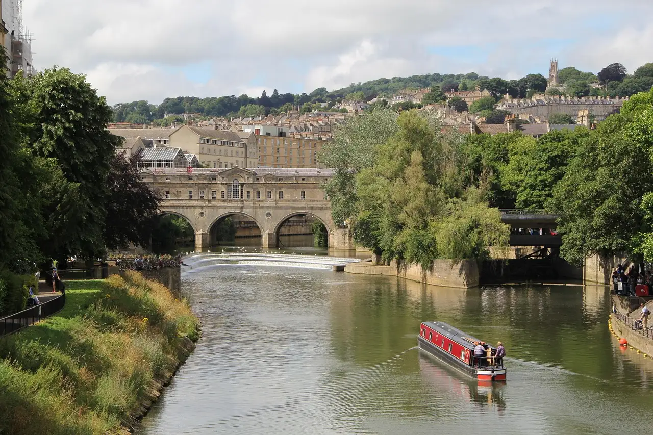 Pulteney Bridge arching over the River Avon in Bath with a red narrowboat on the water and the town rising on the hill behind