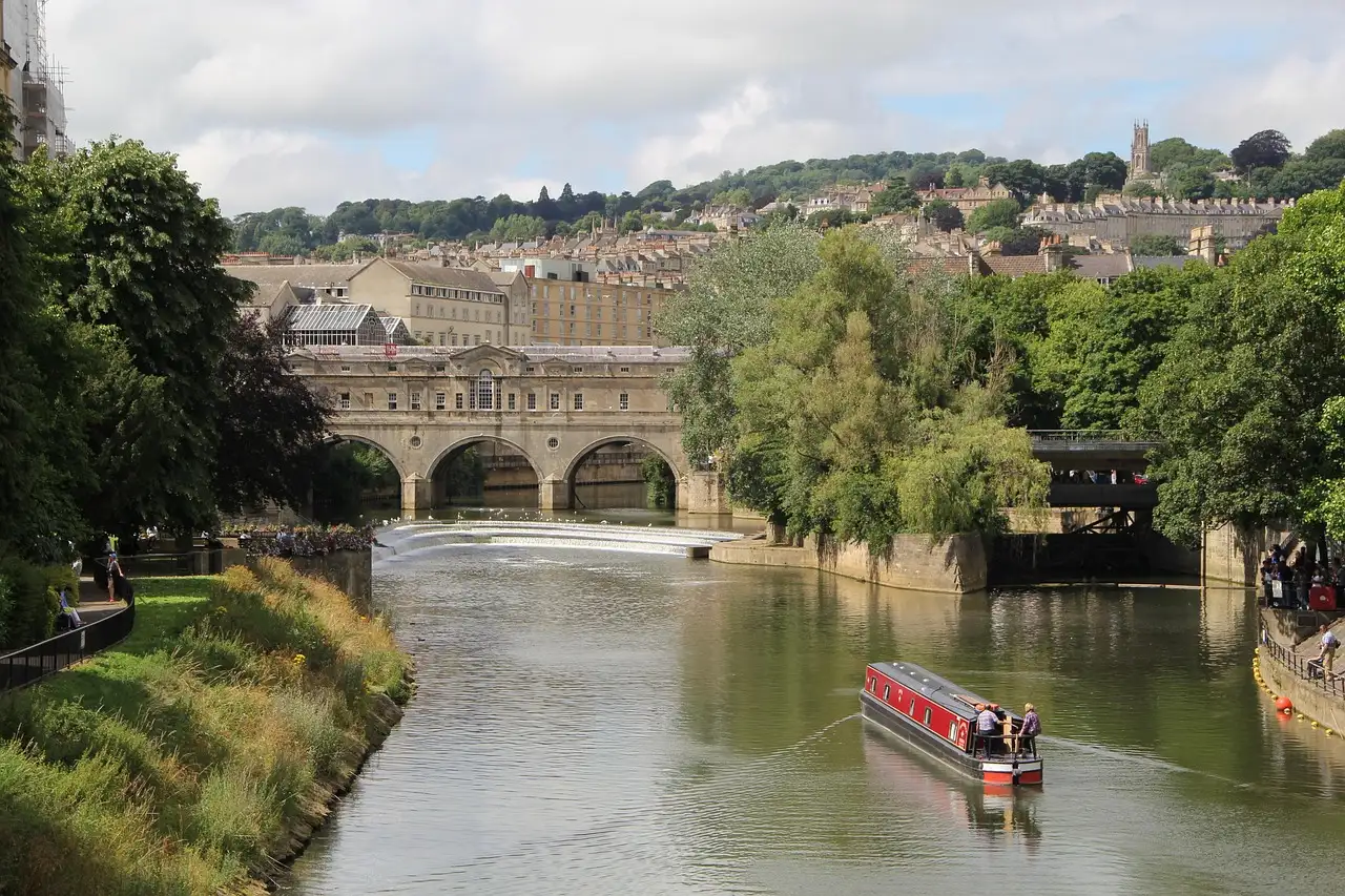 Pulteney Bridge arching over the River Avon in Bath with a red narrowboat on the water and the town rising on the hill behind