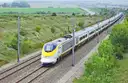 A yellow-nosed Eurostar high-speed train running along a track through green countryside