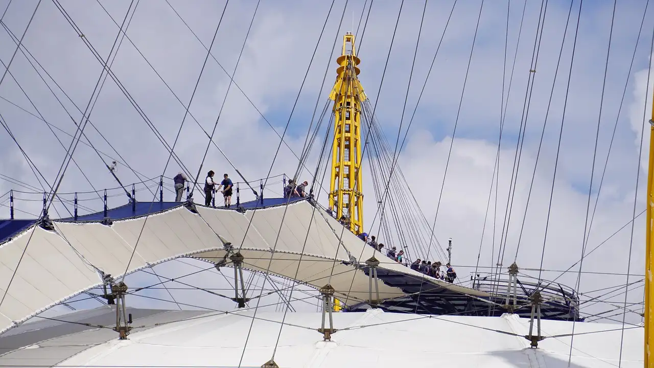 Climbers on the walkway across the white roof of The O2, between yellow masts and cables