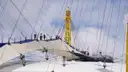 Climbers on the walkway across the white roof of The O2, between yellow masts and cables