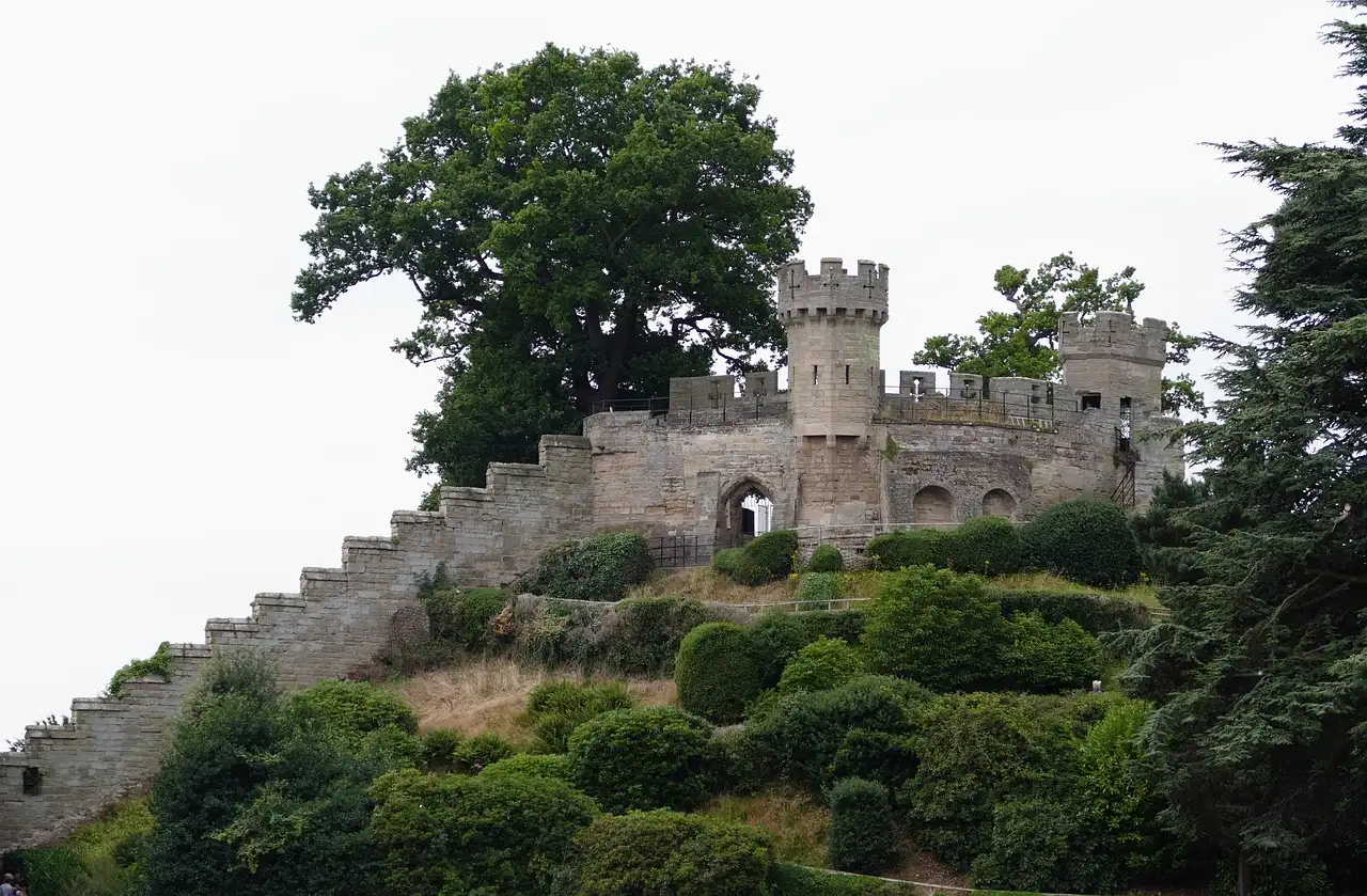 Battlements and towers of Warwick Castle on a tree-covered mound