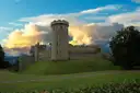 Warwick Castle tower and walls above a green lawn under evening clouds