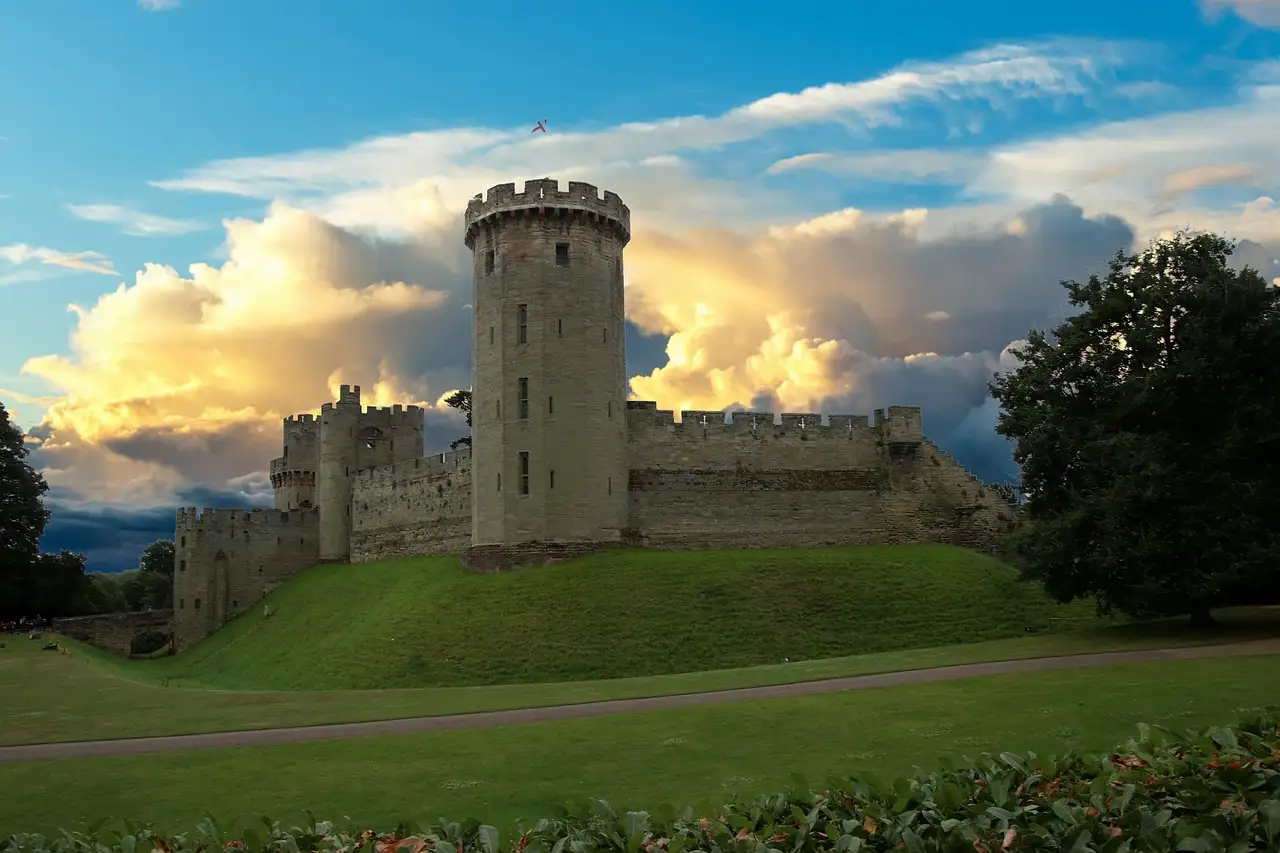 Warwick Castle tower and walls above a green lawn under evening clouds